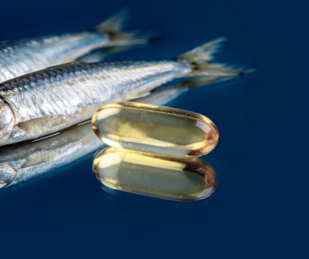 fish oil omega 3 softgel next to sardines in blue background