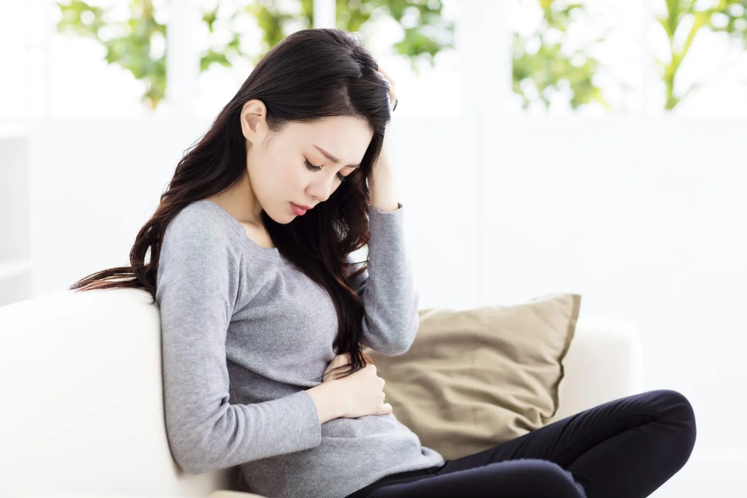A woman in her first trimester with her hand on her belly looking concerned.