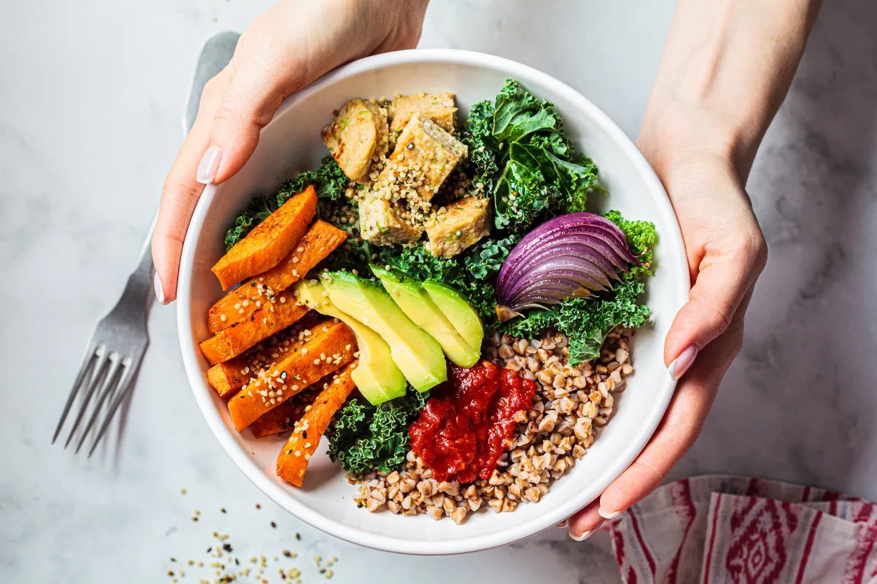 Hands holding a bowl of quinoa, roasted squash, tofu, avocado and kale
