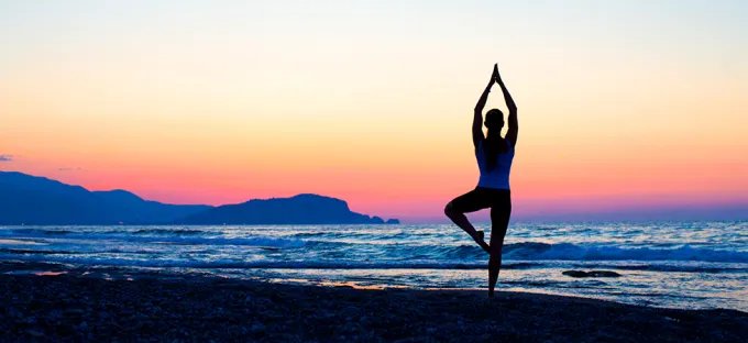Woman practicing yoga in tree pose on a beach at sunset