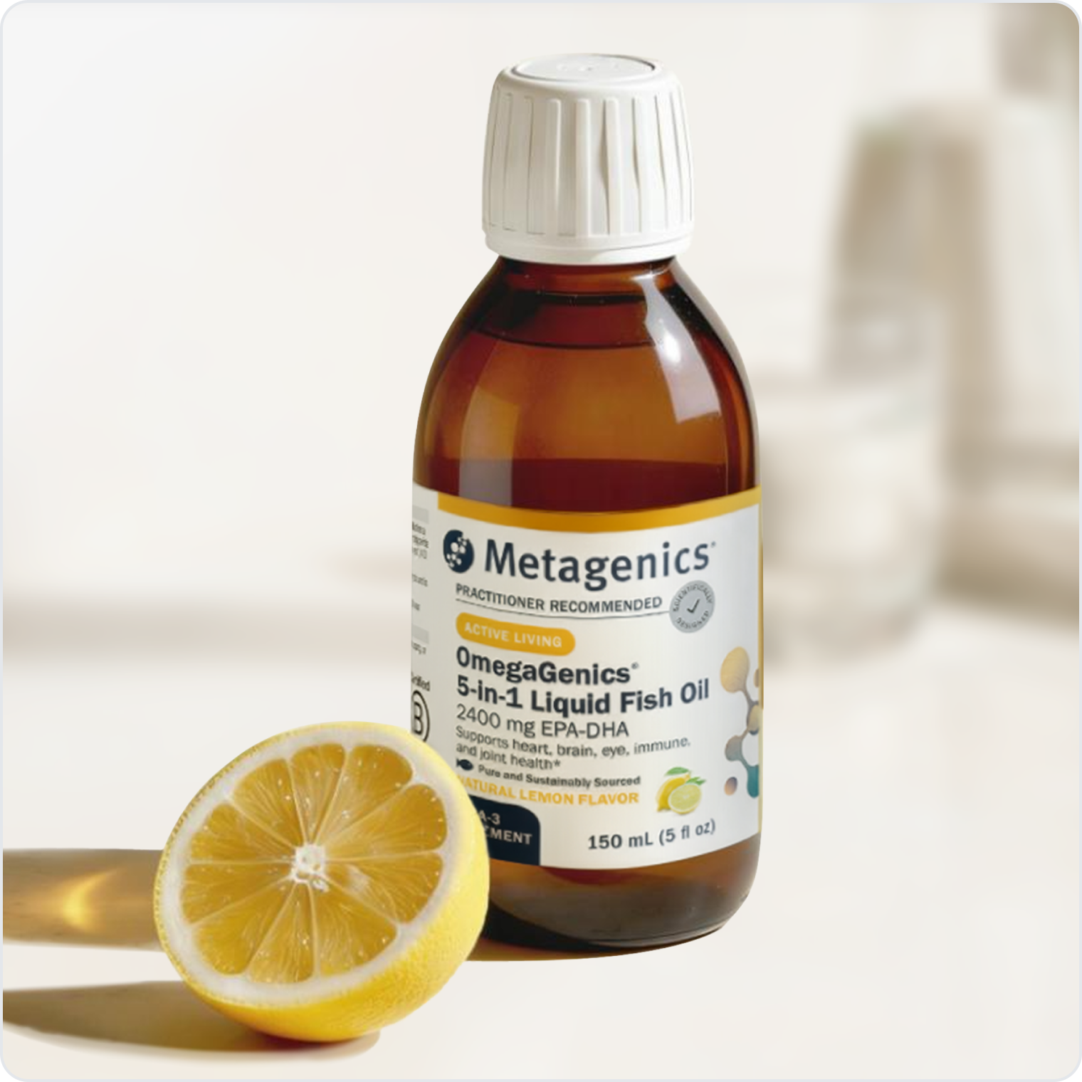 A bottle of Metagenics OmegaGenics® 5‑in‑1 Liquid Fish Oil 2400 mg EPA‑DHA standing beside a half-cut lemon on a light-colored surface with a softly blurred background.
