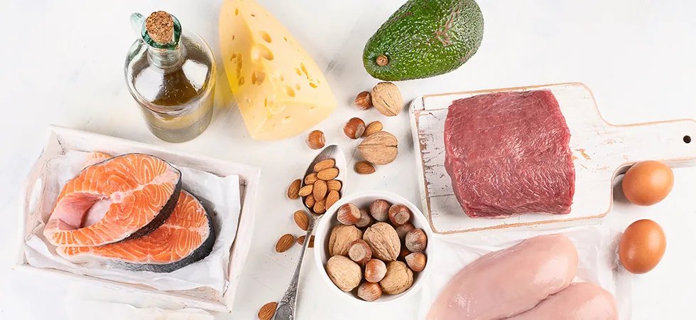 A selection of clean Keto food items including, salmon, vegetable oil, cheese, nuts, avocado, red meat, chicken and eggs