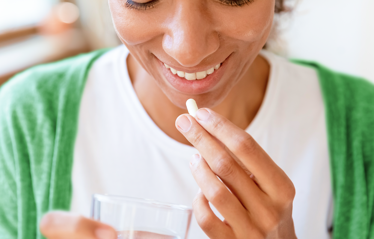 A 30-something Black woman wearing a green sweater and white t-shirt taking UltraFlora Probiotics from Metagenics, premium vitamins and supplements.