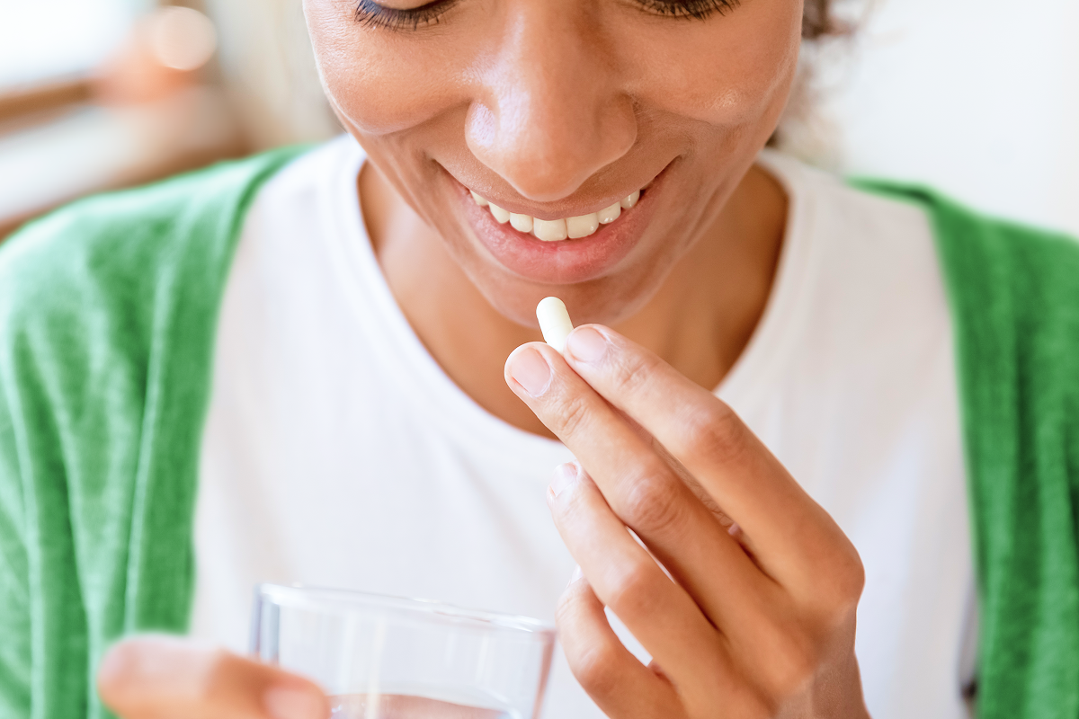 A 30-something Black woman wearing a green sweater and white t-shirt taking UltraFlora Probiotics from Metagenics, premium vitamins and supplements.
