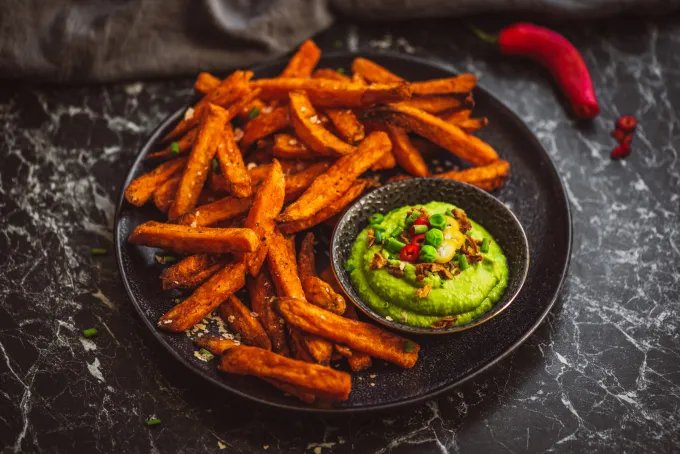 Closeup of a plate of seasoned sweet potato fries with avocado dip on the side