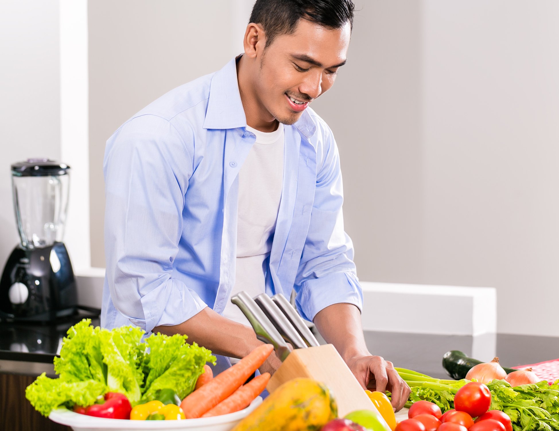 A person smiling while preparing a cutting board full of fresh vegetables, illustrating the importance of fiber intake for gut health. Part of a webpage discussing doctor recommended probiotics and how daily habits influence digestion.