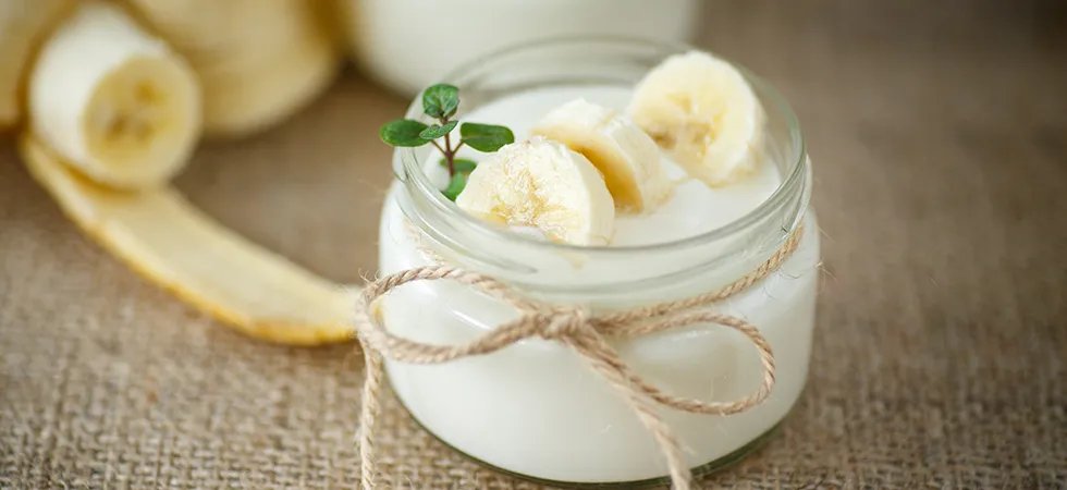 A close up of a small glass jar of yoghurt with sliced bananas