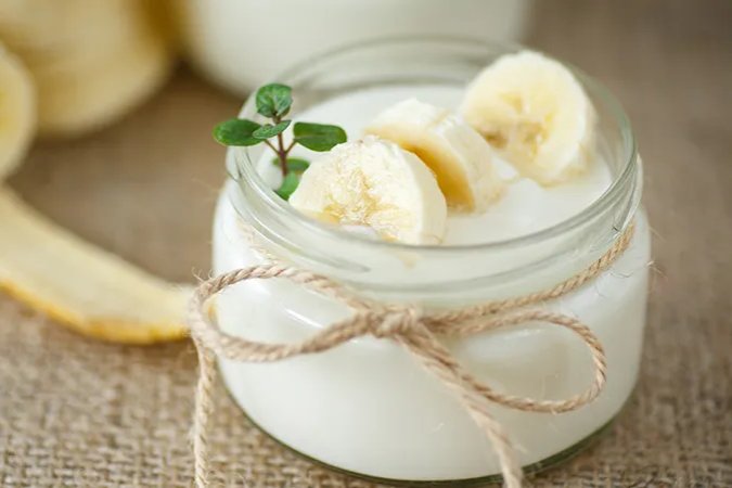 A close up of a small glass jar of yoghurt with sliced bananas
