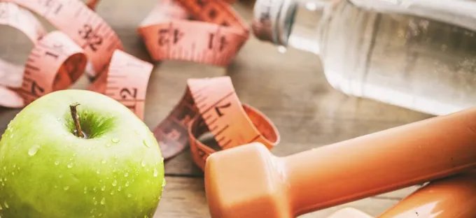 Green apple, measuring tape, dumbbell, and water bottle representing healthy weight management and fitness