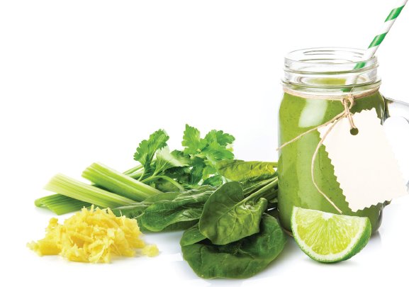 A closeup of a glass with an green colored smoothie with spinach, celery, ginger and lime