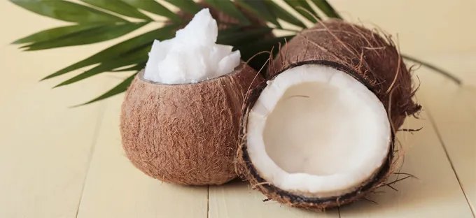 Fresh coconuts on a table top cut in half showing the fresh coconut flesh with a palm leaf in the background
