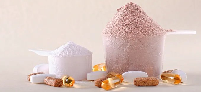Scoops of powdered nutritional products surrounded by tablets and softgel capsules.