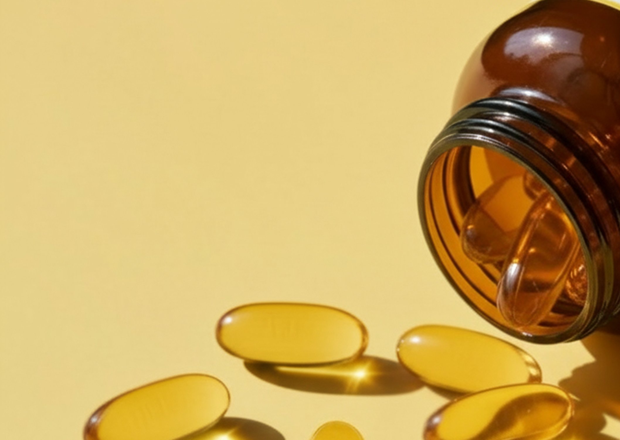 Omegagenics fish oil vitamins & supplements with golden softgel capsules spilling from an amber bottle.