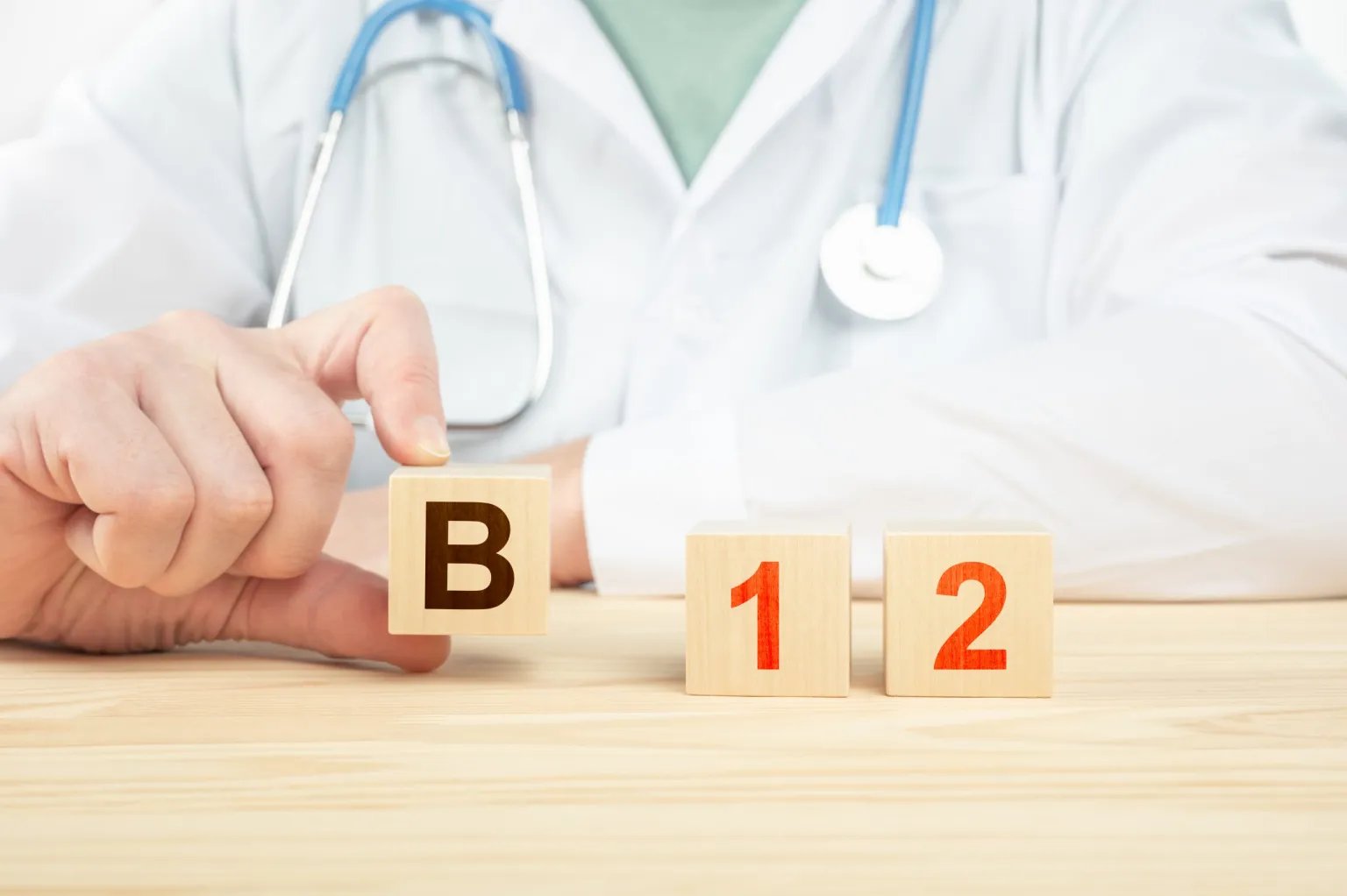 A man wearing a white coat and stethoscope holding toy blocks with the B 12