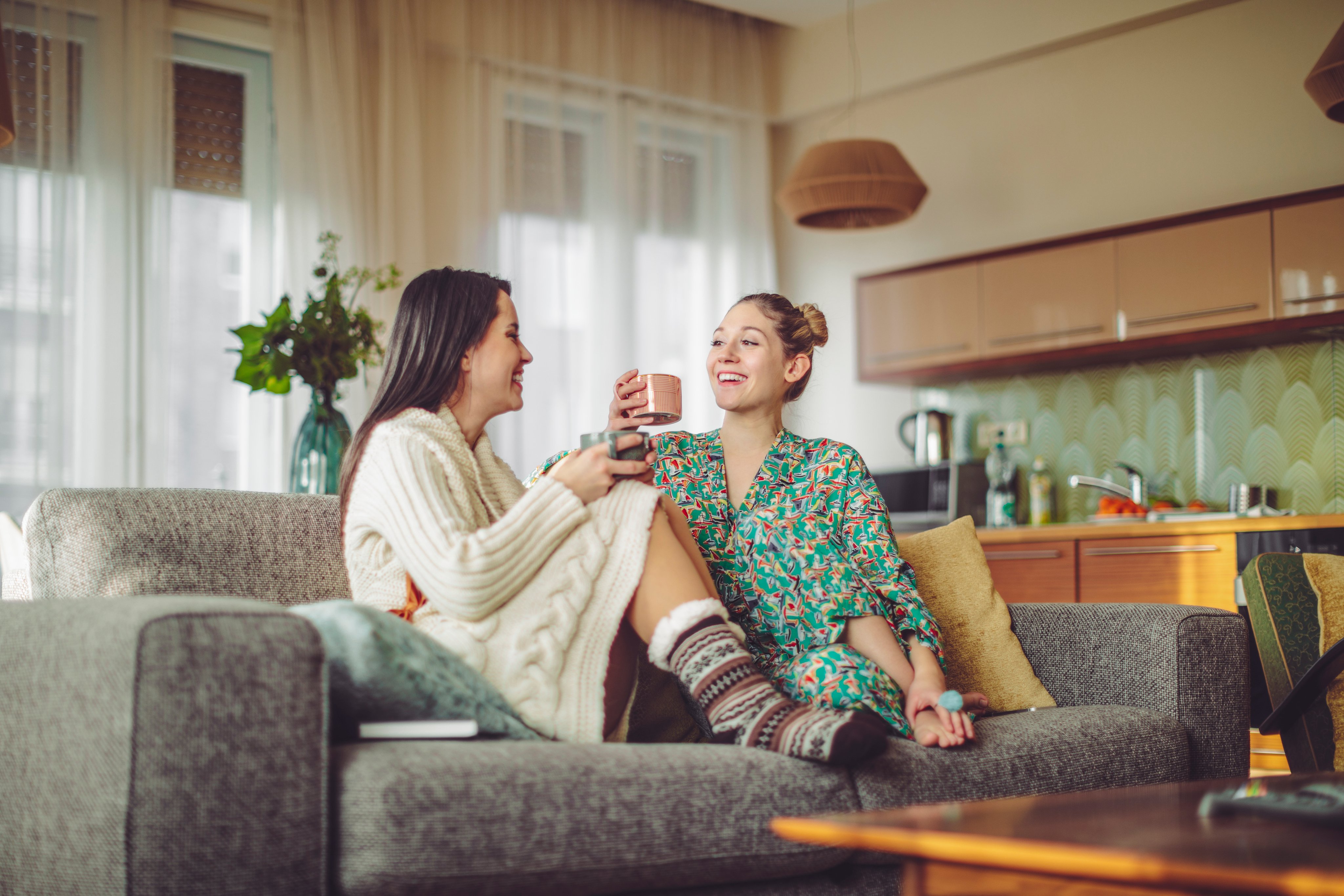 Two young women in loungewear drinking tea at home.