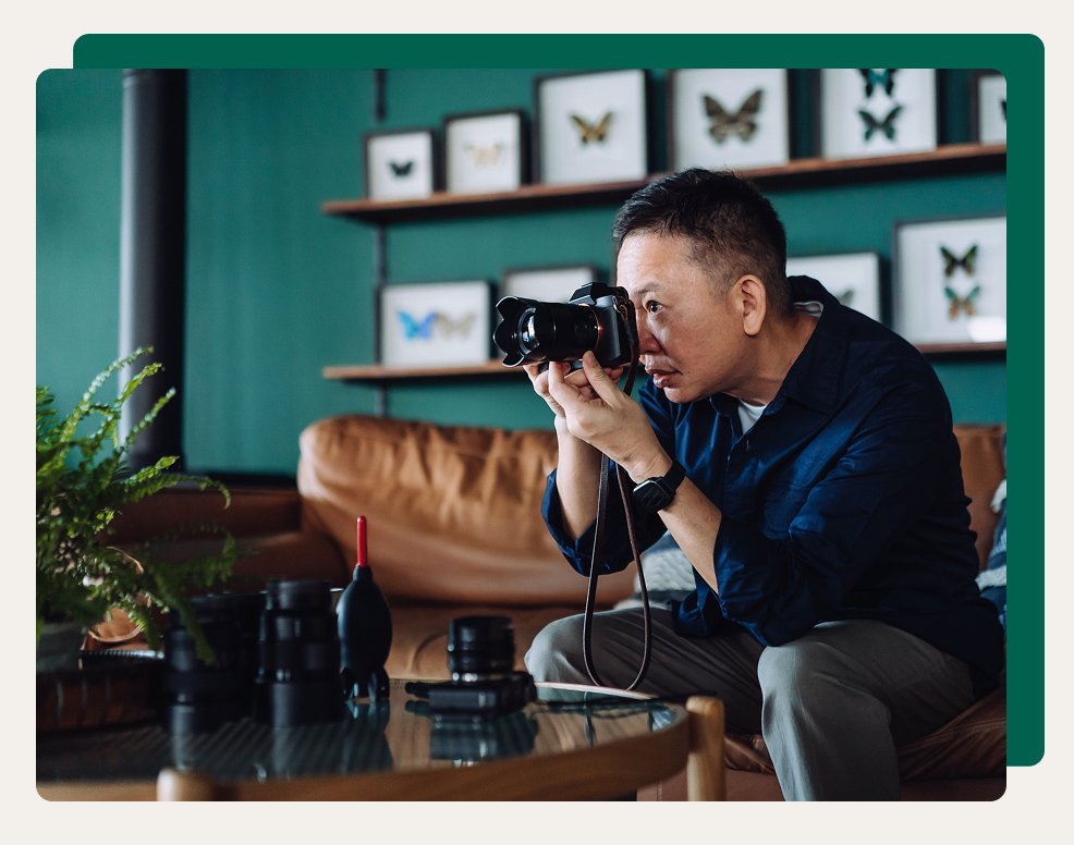 Person using a camera while sitting in a living room with photography equipment on a table.