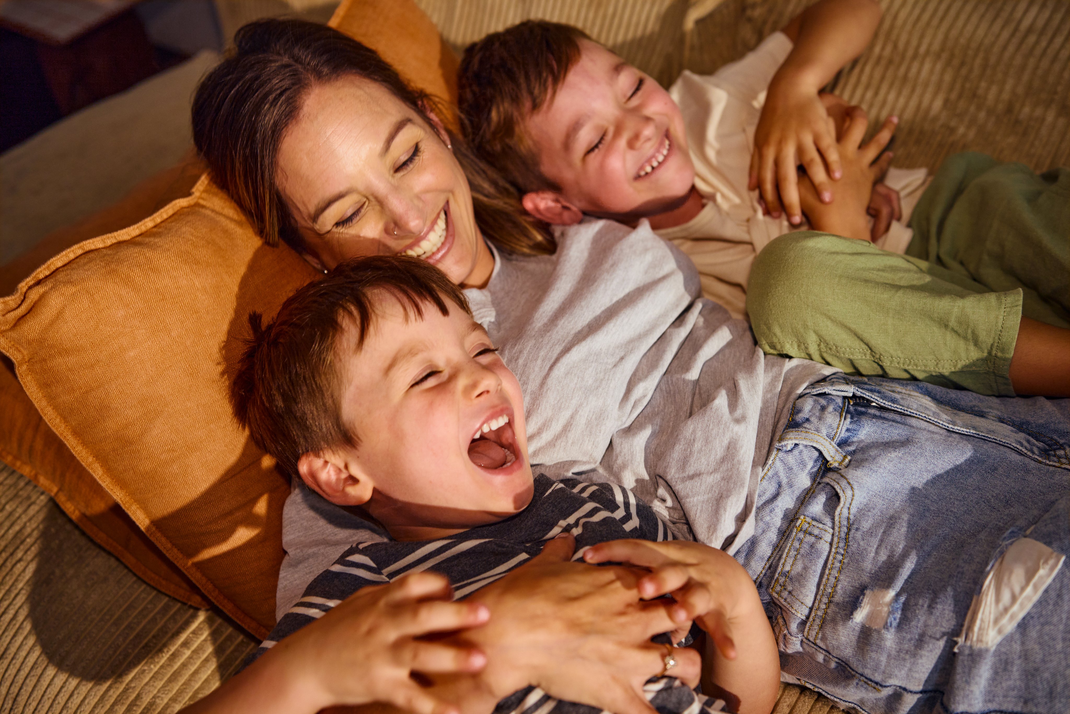 Mother and children playing and laughing together on sofa at home