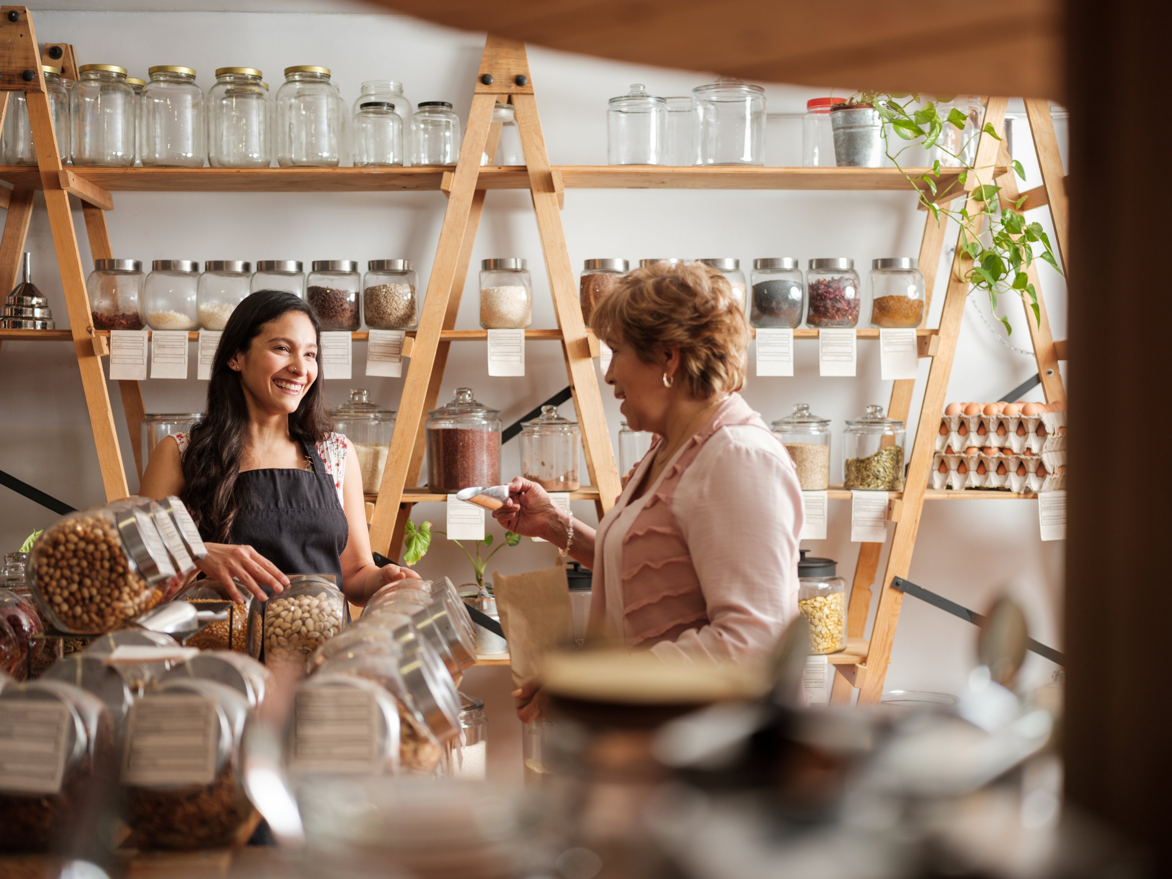Happy employee and senior female customer standing next to the shelves of a sustainable shop and smiling at each other.