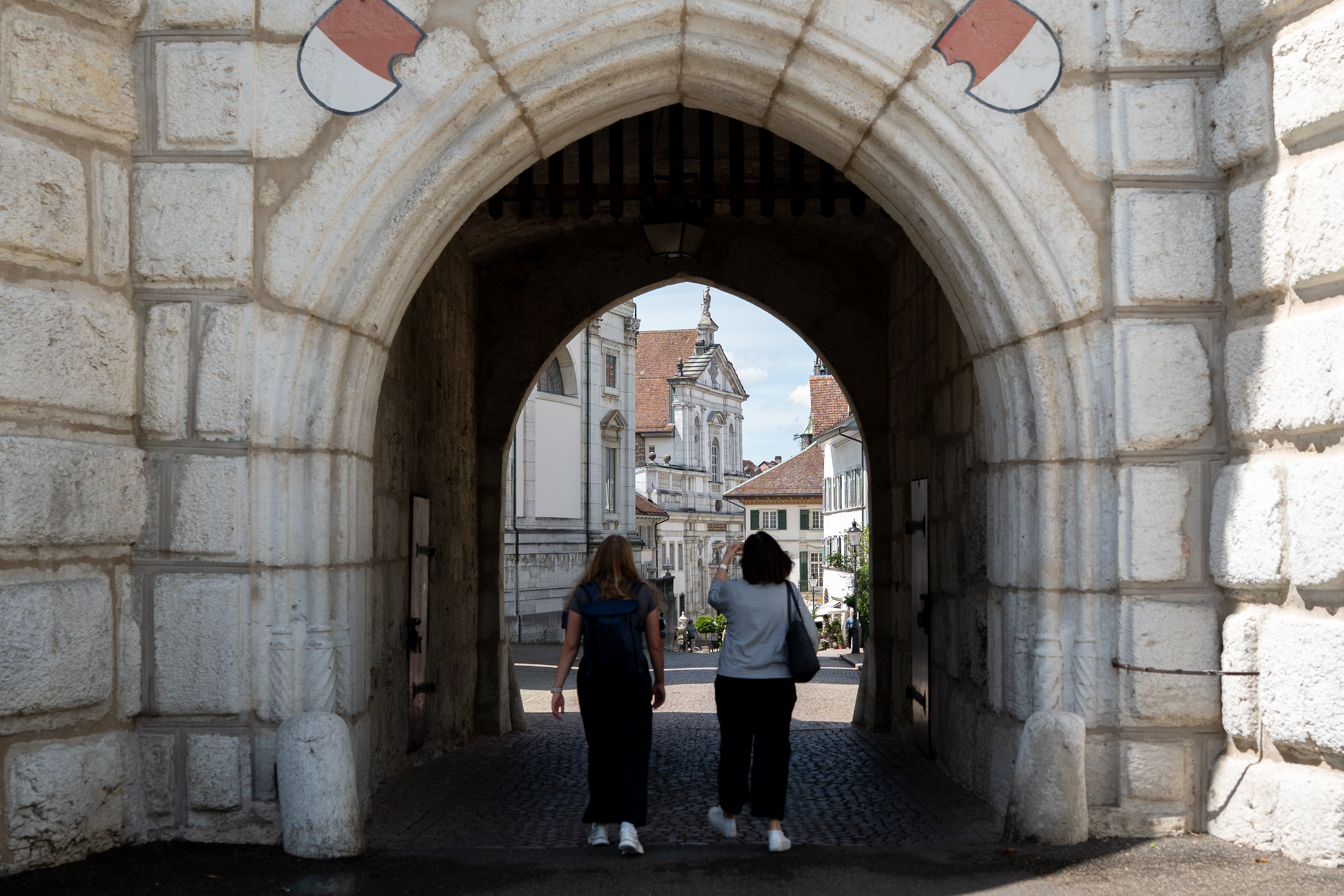 Zwei Personen laufen durch ein grosses Tor mit altem Gemäuer.