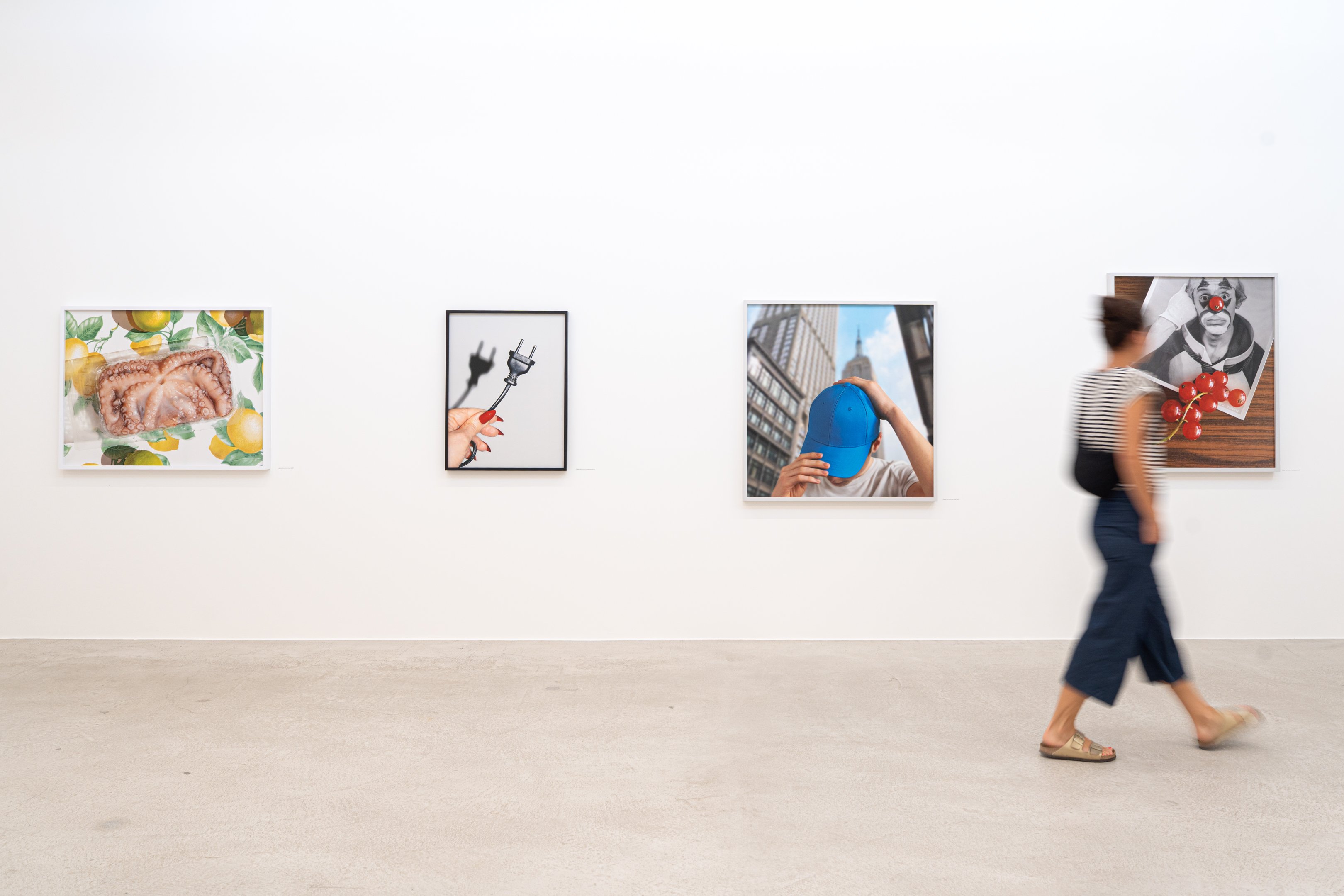 Quatre photos encadrées sur un mur blanc, une femme passe devant.