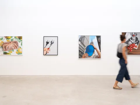Quatre photos encadrées sur un mur blanc, une femme passe devant.