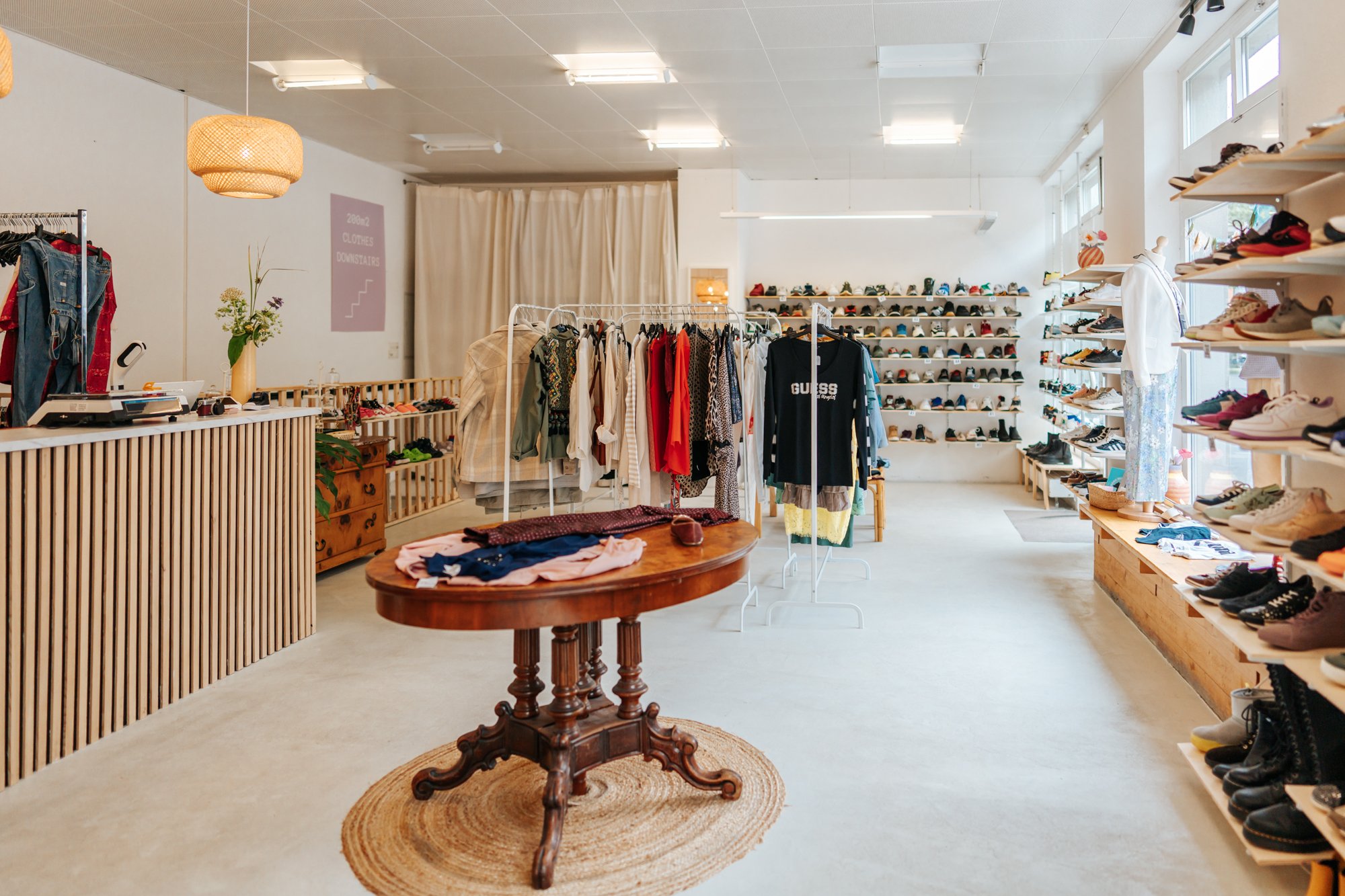 Ein schlicht eingerichteter Kleiderladen mit Schuhen und aufgehängten Jacken.