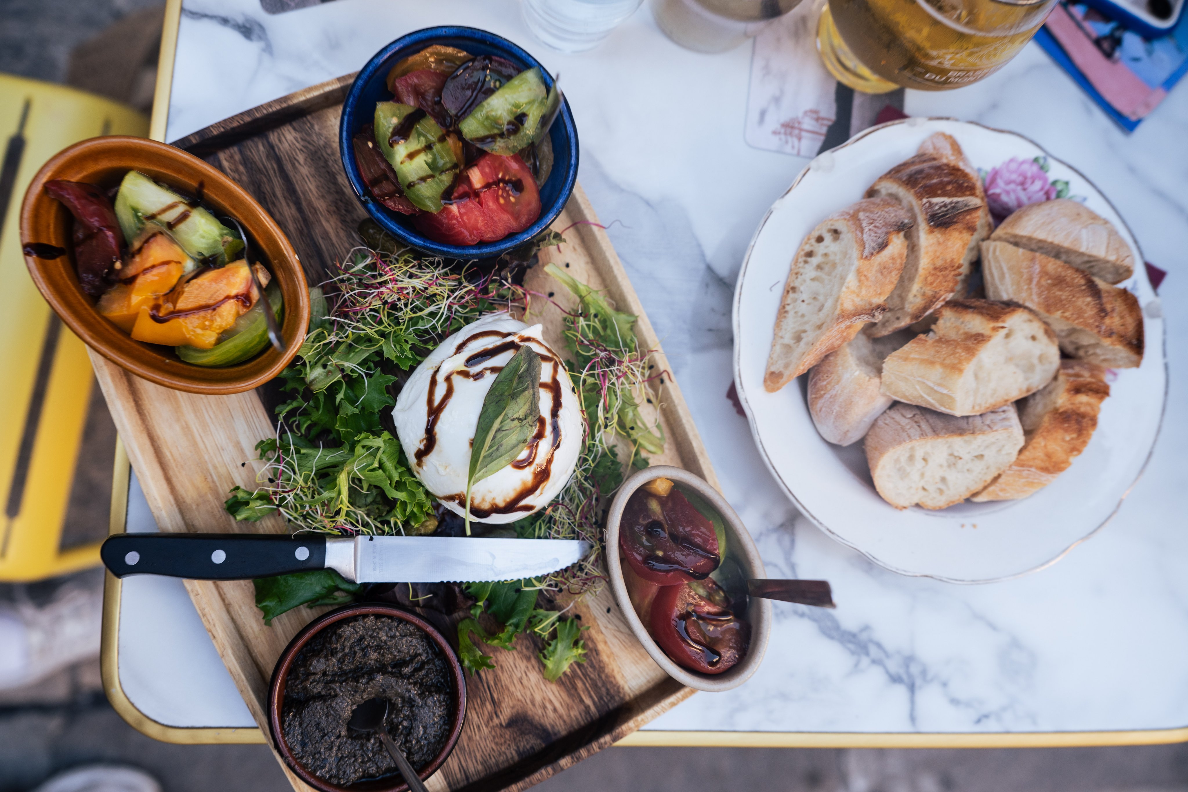 Su un tagliere di legno sono serviti pomodori, formaggio e altre specialità con un contorno di pane. 