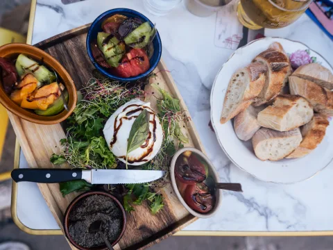 Su un tagliere di legno sono serviti pomodori, formaggio e altre specialità con un contorno di pane.