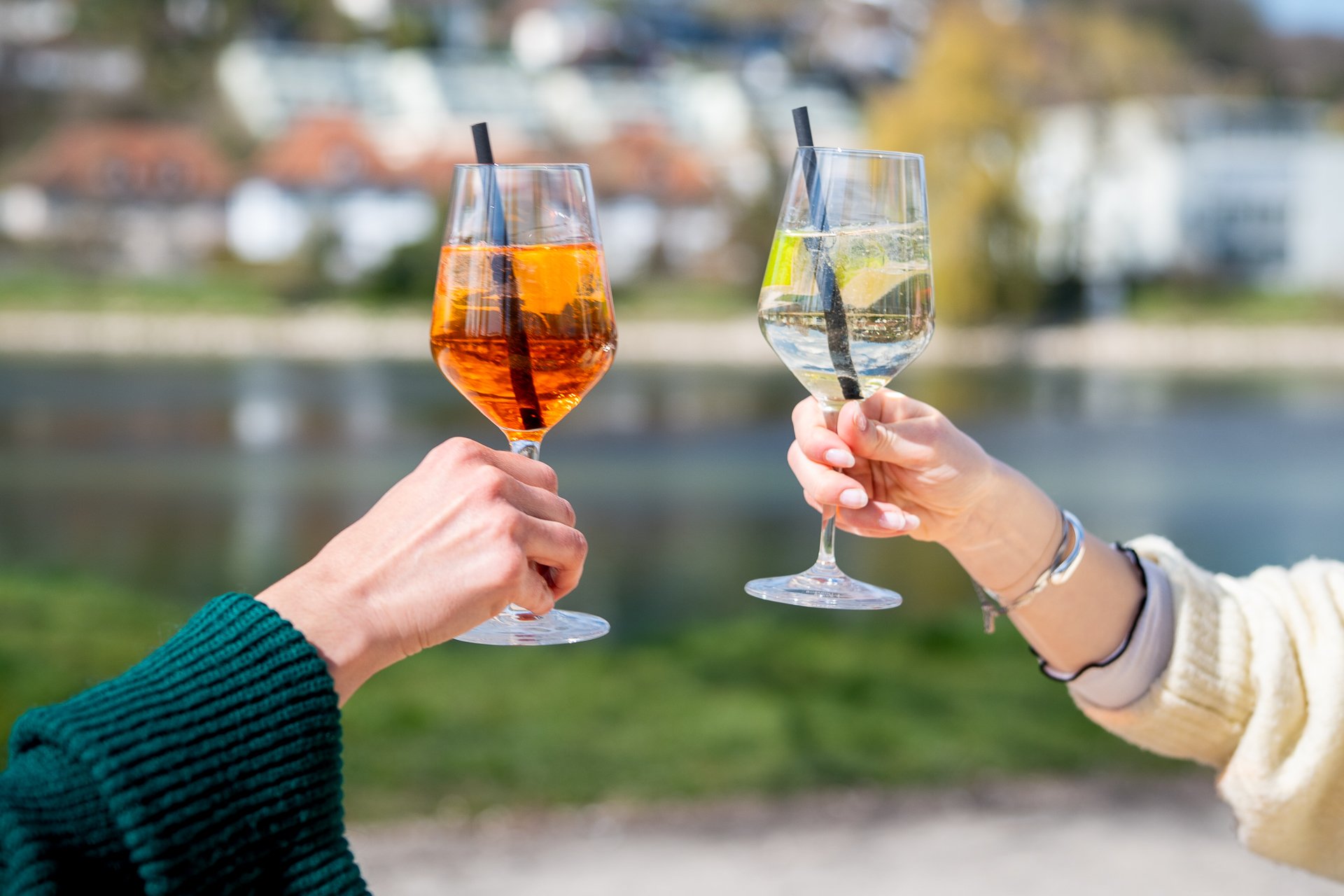 Zwei Personen stossen mit Getränken an. Im Hintergrund fliesst der Fluss Aaare vorbei.