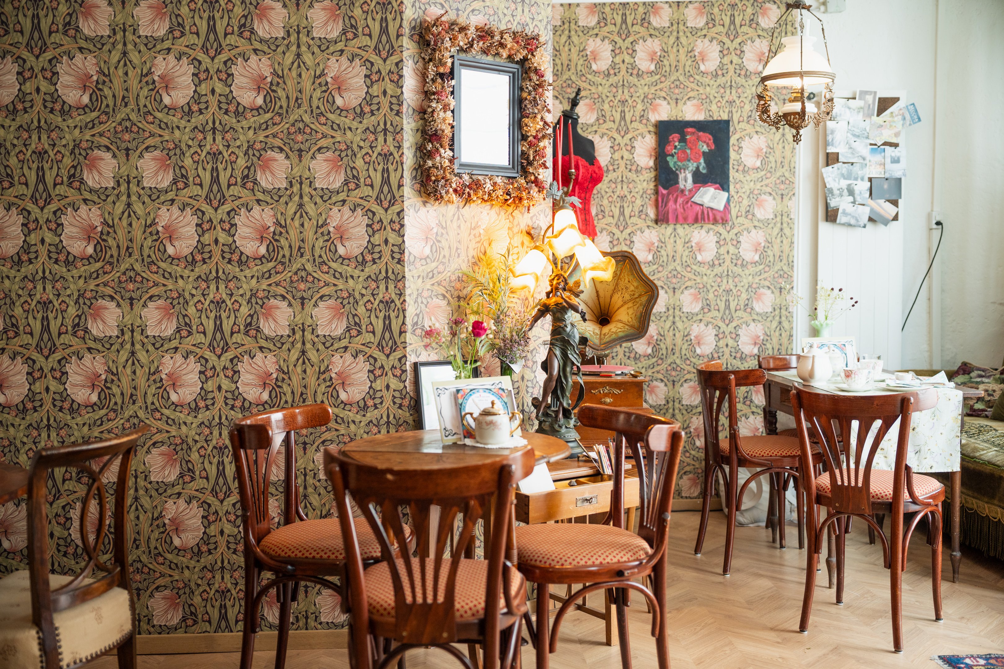 Tables et chaises anciennes dans la salle du café, devant des murs tapissés à motif floral.