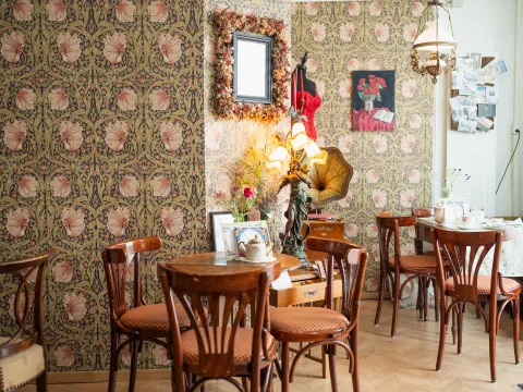 Tables et chaises anciennes dans la salle du café, devant des murs tapissés à motif floral.