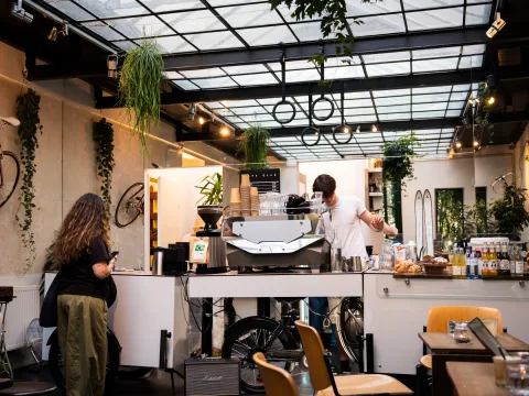 Interno del Cafe Glas a Vienna con macchina per caffè espresso, piante e arredi moderni. Una donna aspetta il caffè davanti al bancone.