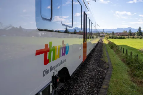 Seitenansicht eines Thurbo Zugs unterwegs im Grünen.