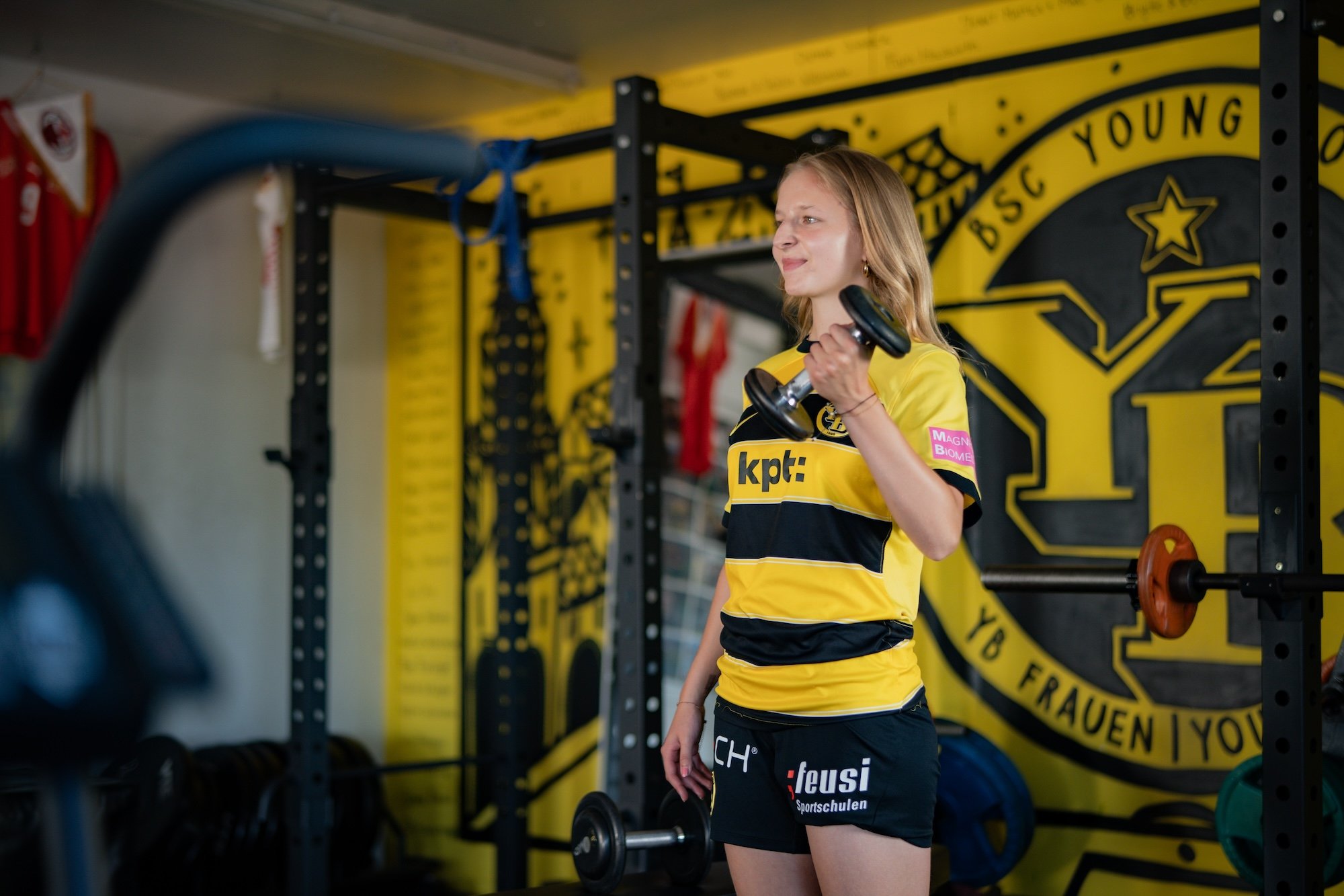 Una donna in tenuta sportiva solleva un manubrio con la mano sinistra.