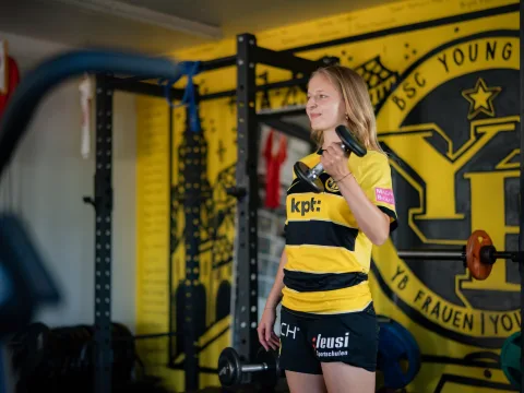 Una donna in tenuta sportiva solleva un manubrio con la mano sinistra.