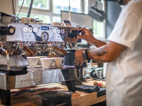 Inhaber Cem steht an der Kaffeemaschine und macht Milchschaum.