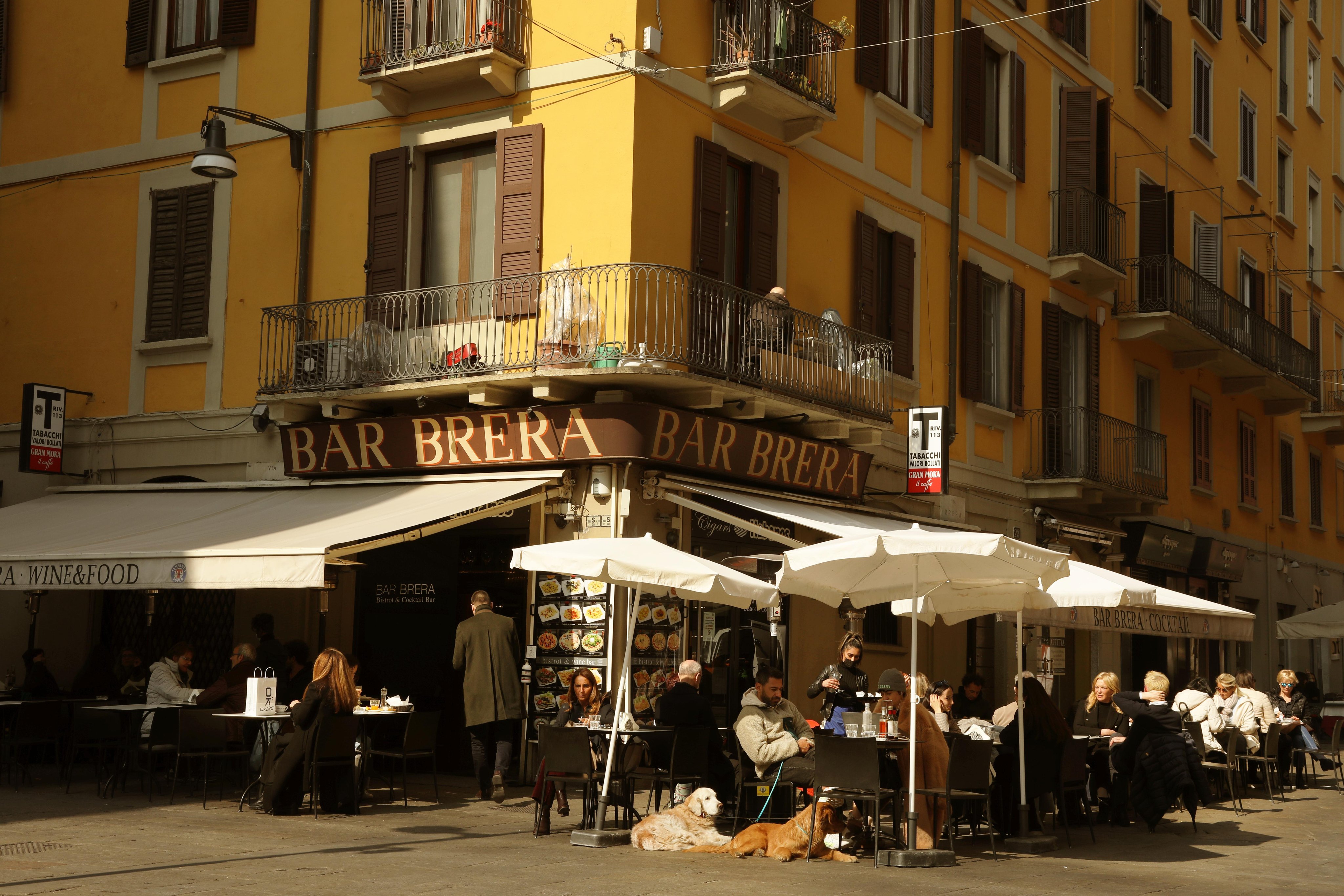 Angolo della strada con un bar che ha sistemato tavoli, sedie e ombrelloni all’aperto.