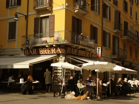 Angolo della strada con un bar che ha sistemato tavoli, sedie e ombrelloni all’aperto.