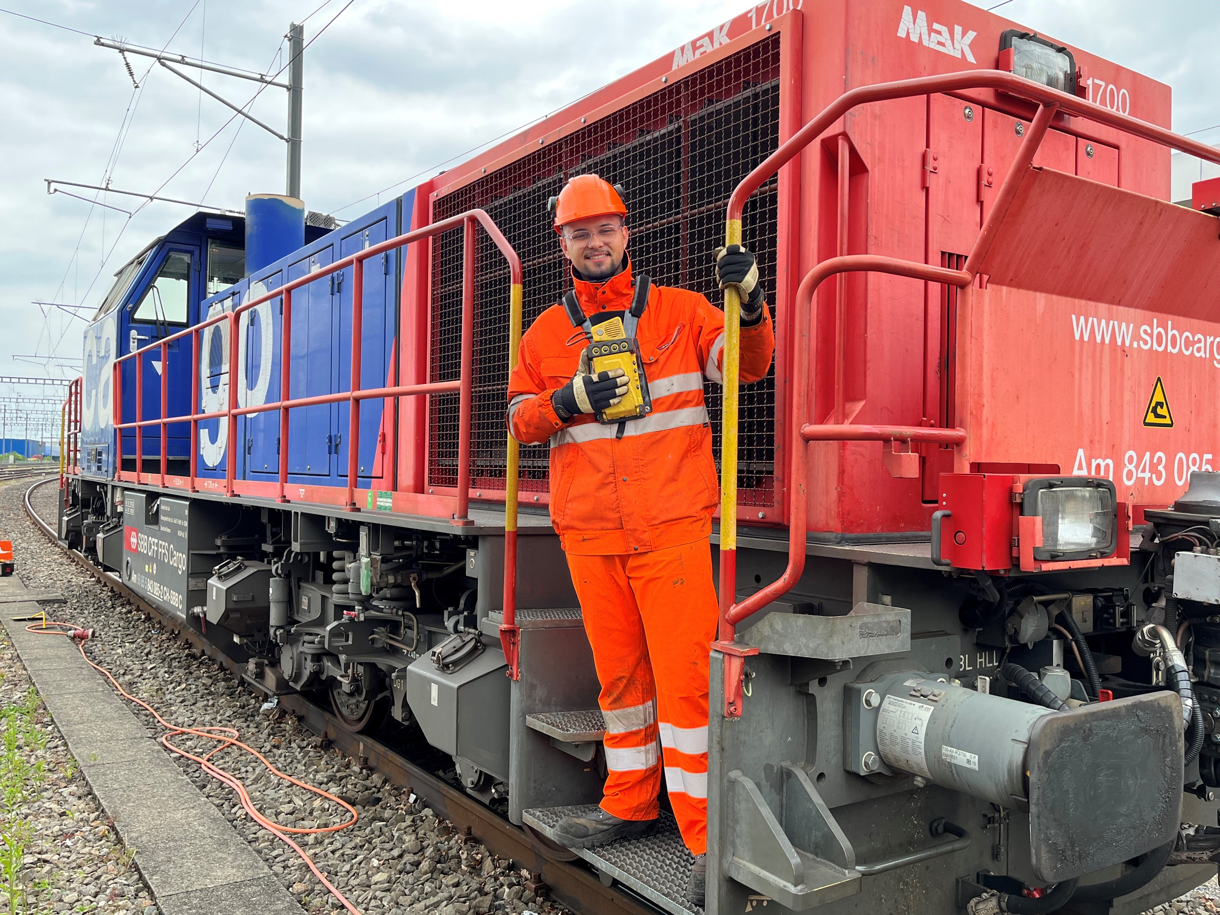 Rangierspezialisten Sabit Medi steht auf dem Trittbrett der Rangierlok Am 843 und hält sich an der Haltestange fest.