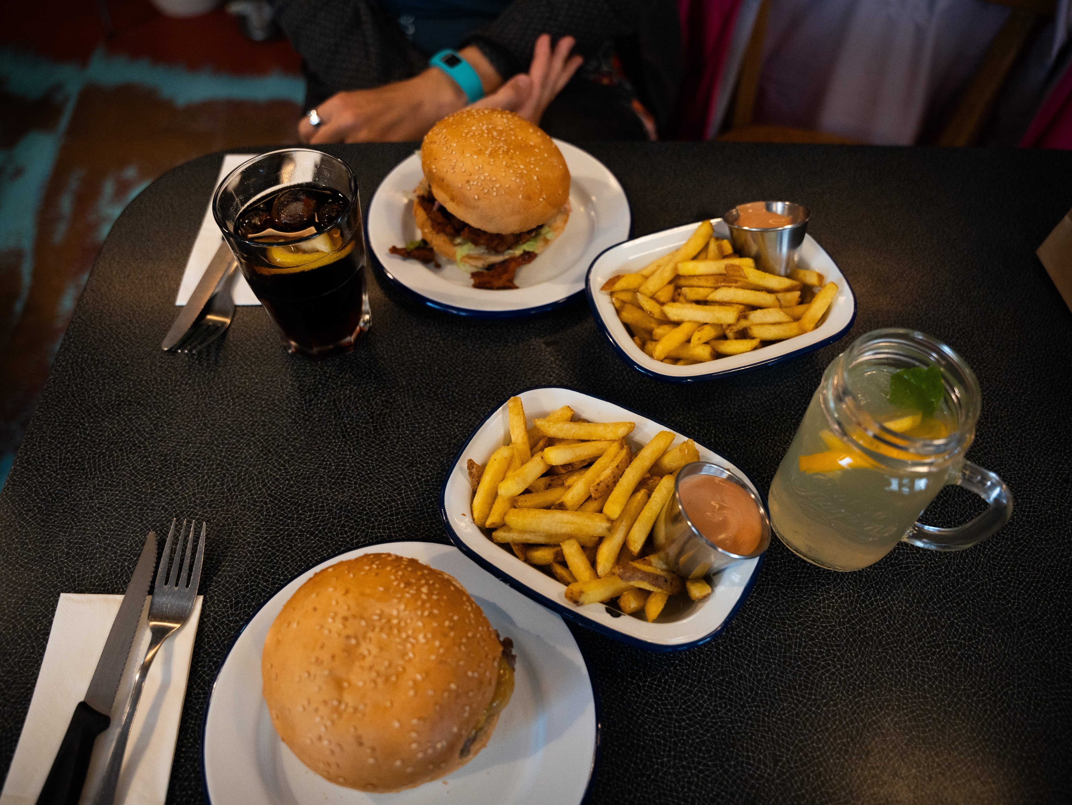 Des assiettes et bols contenant des hamburgers, de la salade et des frites se trouvent sur une table, accompagnés de deux verres pleins.