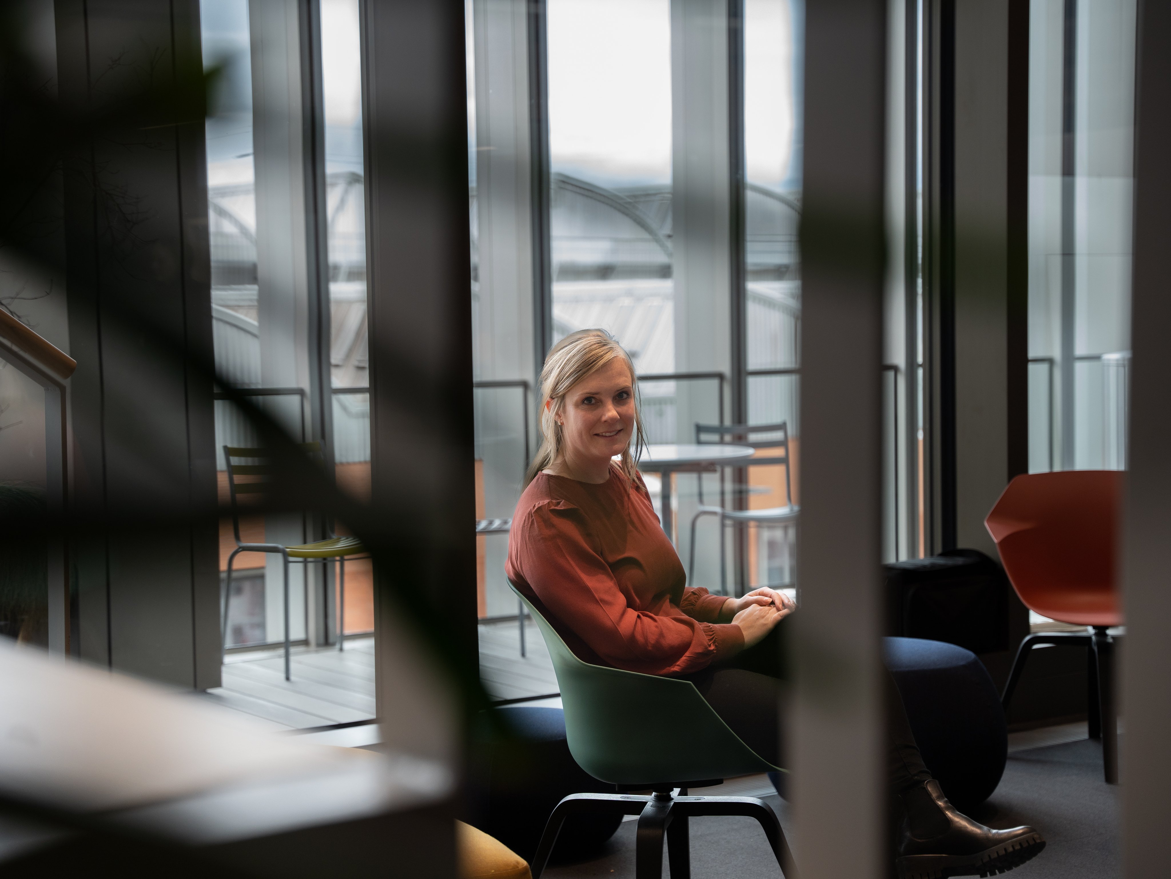 Sandra Schwander sitzzt auf einem grünen Stuhl und schaut in die Kamera. Sie hat einen roten Pullover an. 