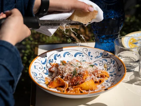 Mains râpant du parmesan au-dessus d’un bol de pâtes italiennes et motif de vaisselle rehaussant le charme du plat.