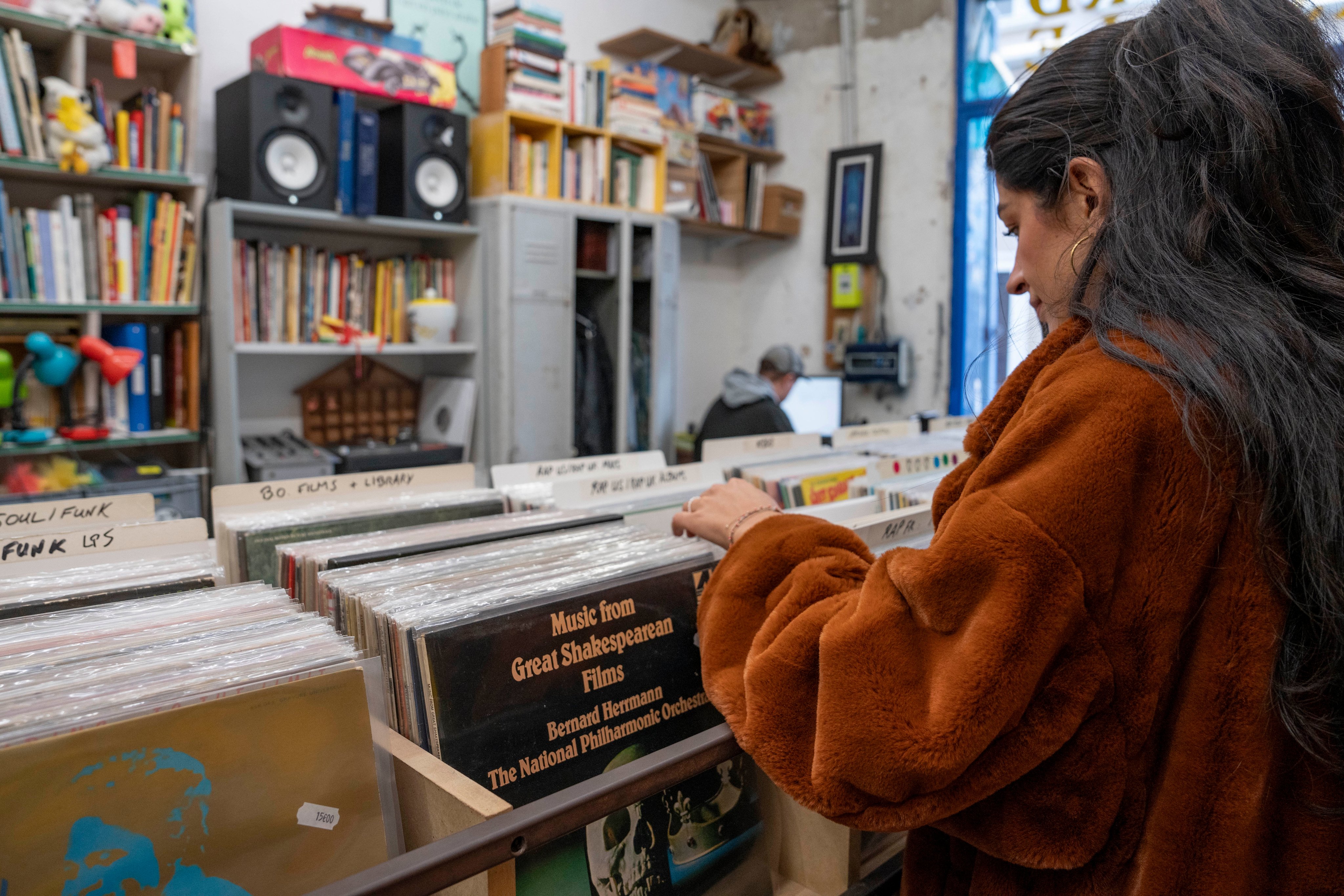 Une personne fouillant méthodiquement la collection de disques en vinyle dans une petite boutique remplie de livres et de musique.