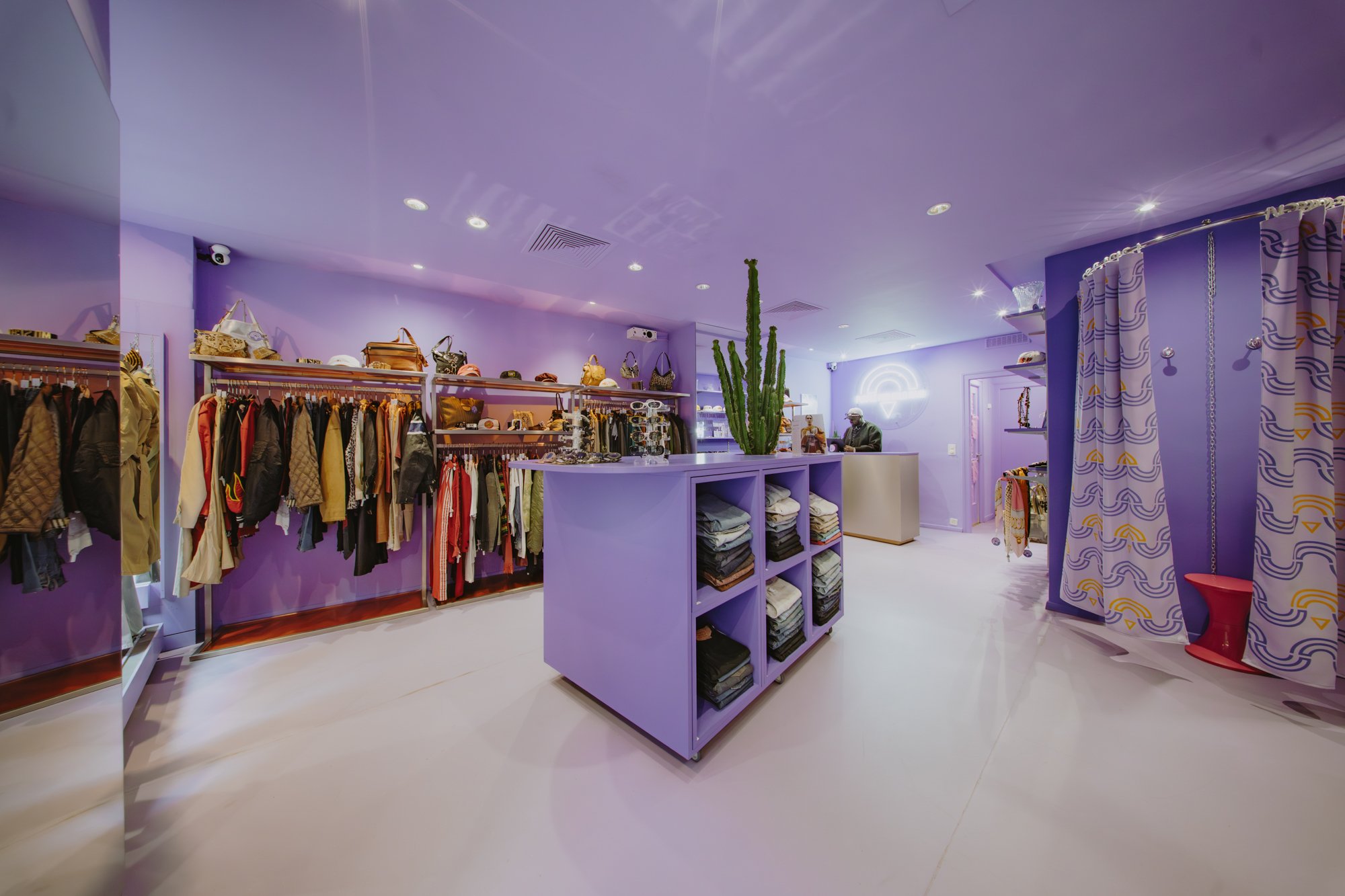 Intérieur de la boutique genevoise Purple and Gold Rain avec murs d’un violet intense, vêtements colorés et décoration pleine de style.