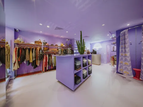 Intérieur de la boutique genevoise Purple and Gold Rain avec murs d’un violet intense, vêtements colorés et décoration pleine de style.