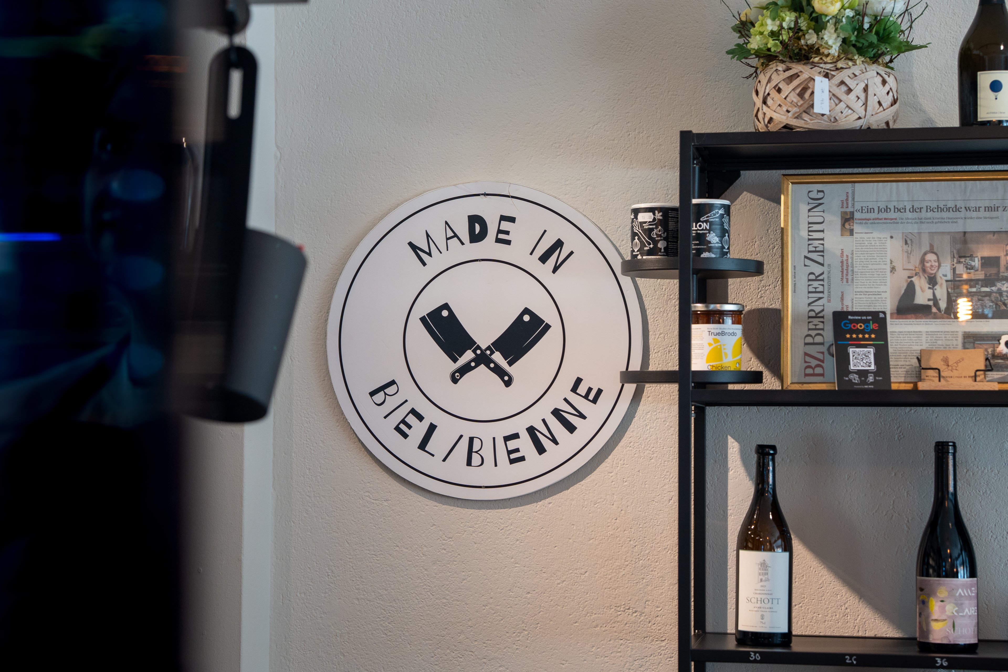 Su una parete è appesa un’insegna con la scritta «Made in Bienne». Accanto si trova uno scaffale con bottiglie di vino, alimenti in vasetti e un articolo di giornale incorniciato.