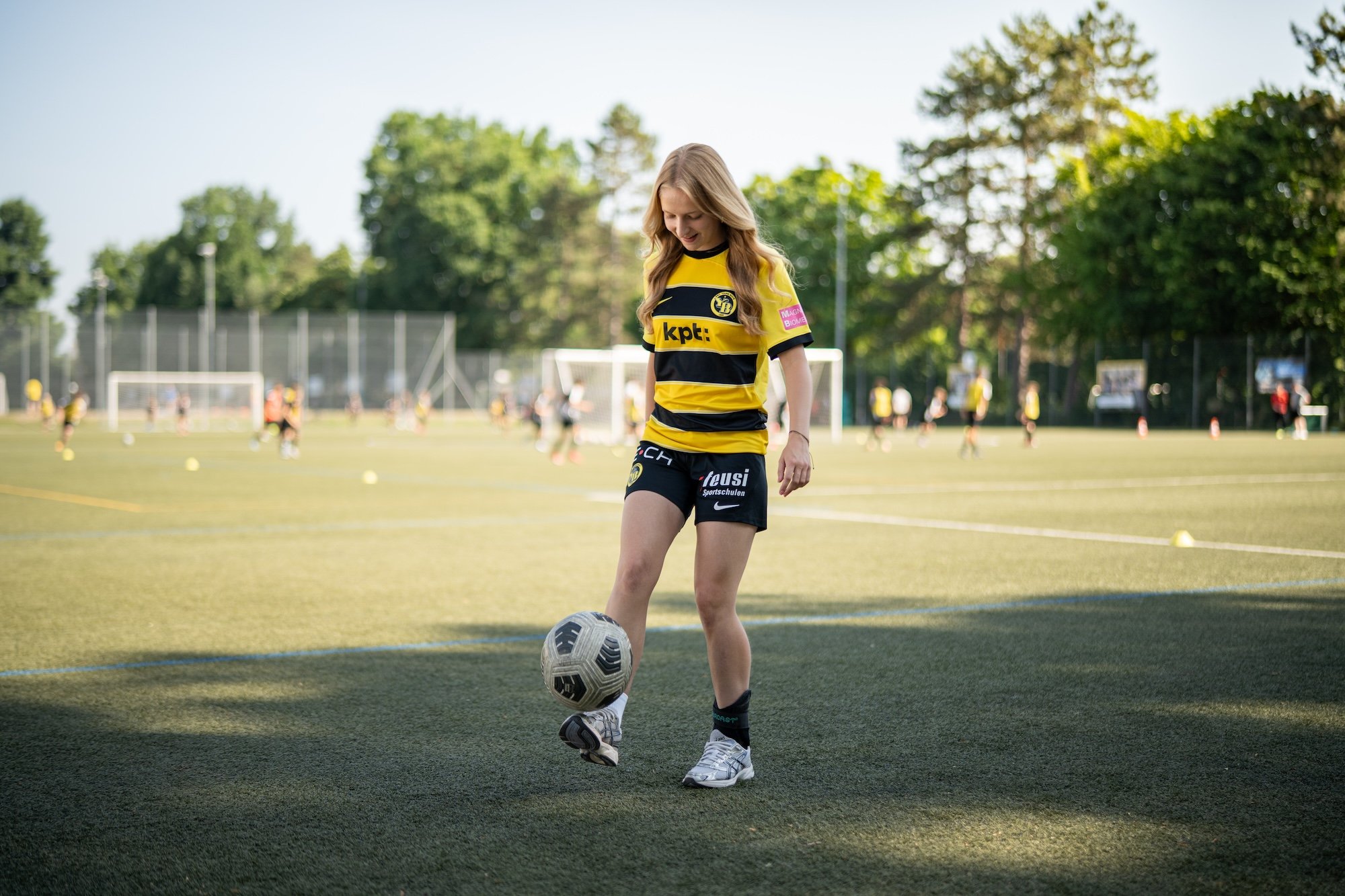 Una donna in tenuta sportiva manovra una palla sui piedi su un campo da calcio.