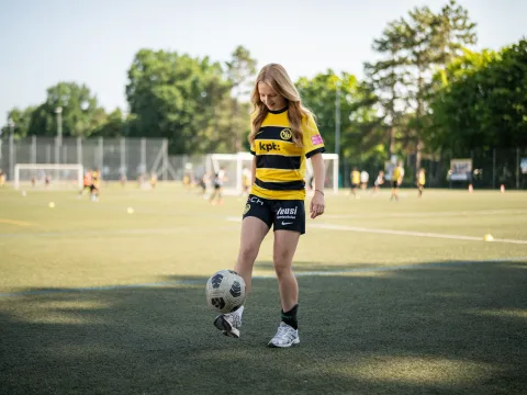 Una donna in tenuta sportiva manovra una palla sui piedi su un campo da calcio.