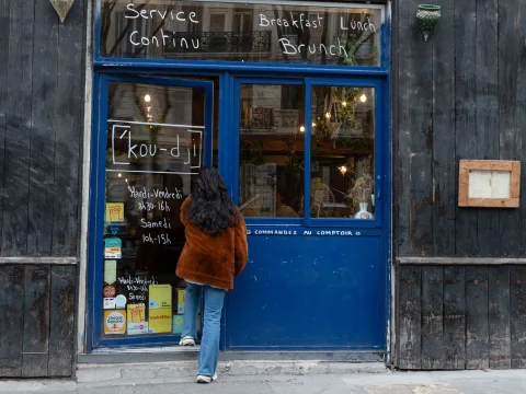 Une personne devant le café Coogee, à Marseille, regardant l’ardoise avec les horaires d’ouverture en continu ainsi que les offres pour le petit-déjeuner, le dîner et le brunch.