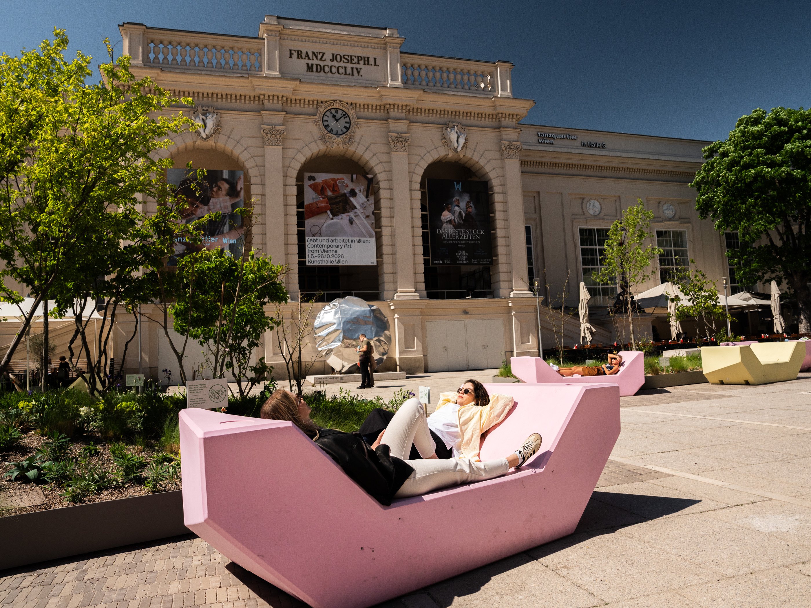 Due donne sono distese sulle panchine rosa nel cortile interno del MuseumsQuartier di Vienna in una giornata di sole.